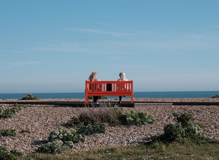 Two people sitting on a red bench on the seafront